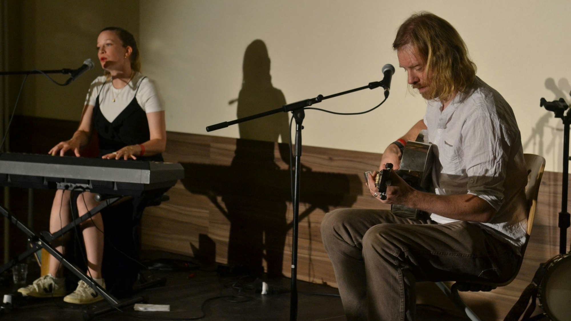 Kirsty Merryn sitzt an einem Keyboard und singt, Ben Walker begleitet sie auf einer Gitarre.