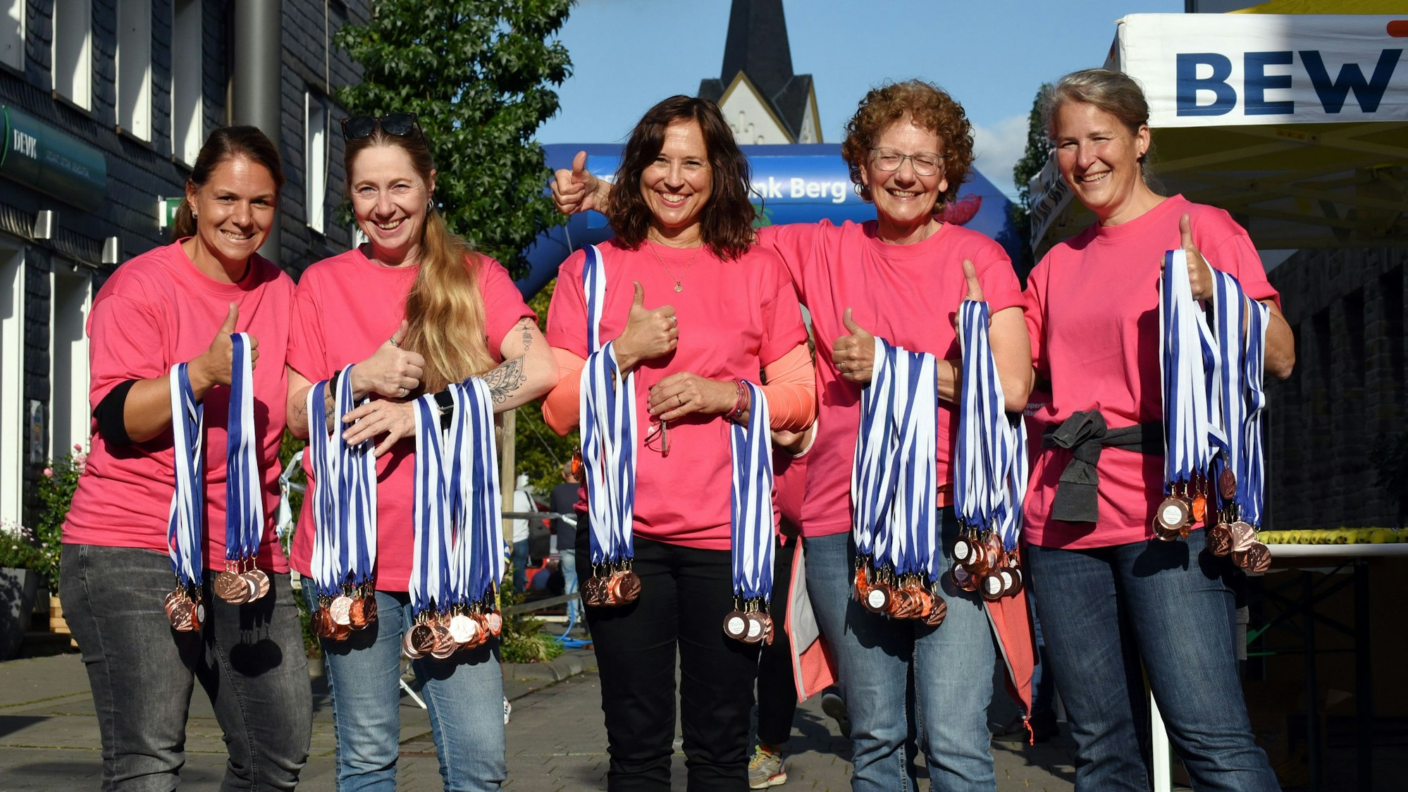Mehrere Frauen in pinken T-Shirts stehen nebeneinander und halten viele Medaillen in den Händen.