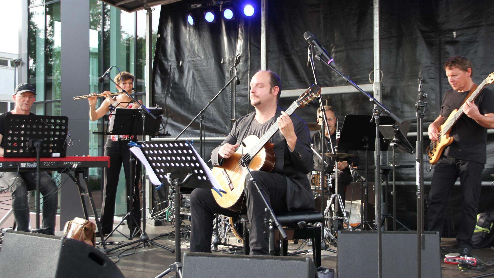 Eine Band mit Piano, Querflöte, akustischer Gitarre, Schlagzeug und Bass auf der Bühne