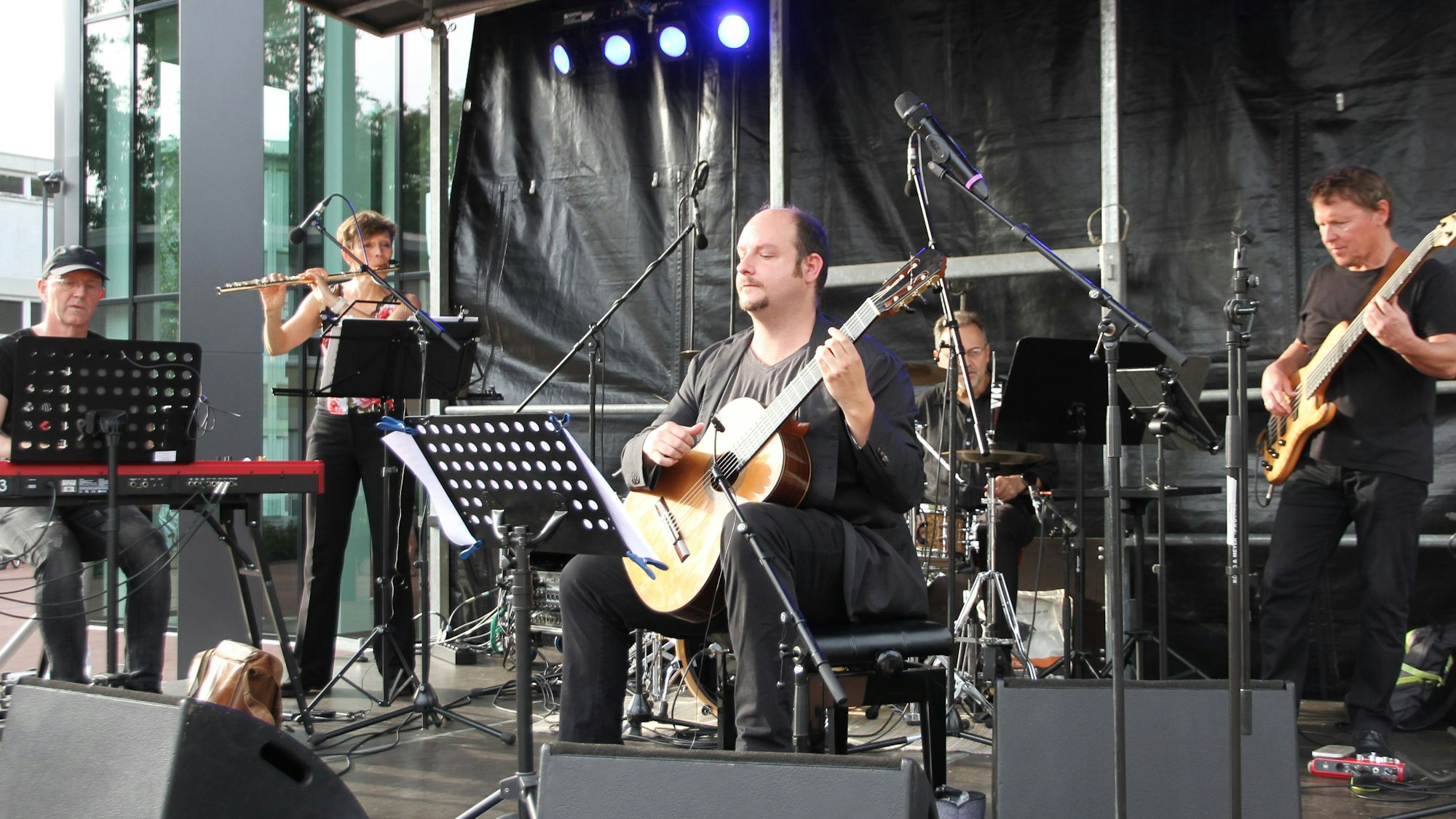 Eine Band mit Piano, Querflöte, akustischer Gitarre, Schlagzeug und Bass auf der Bühne