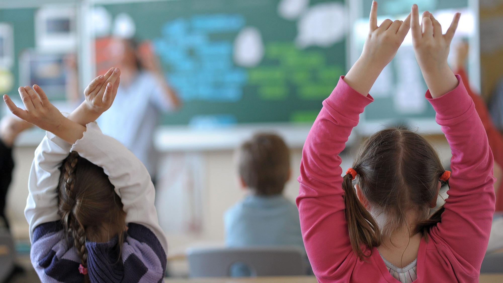 Zwei Schülerinnen melden sich während des Unterrichts in einem Klassenzimmer einer Grundschule.