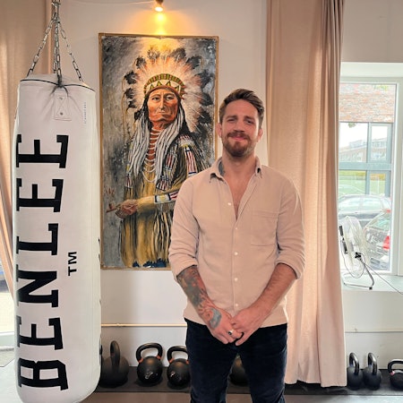 Ein Mann mit Bart steht vor einem Bild von einem Indianerhäuptling.