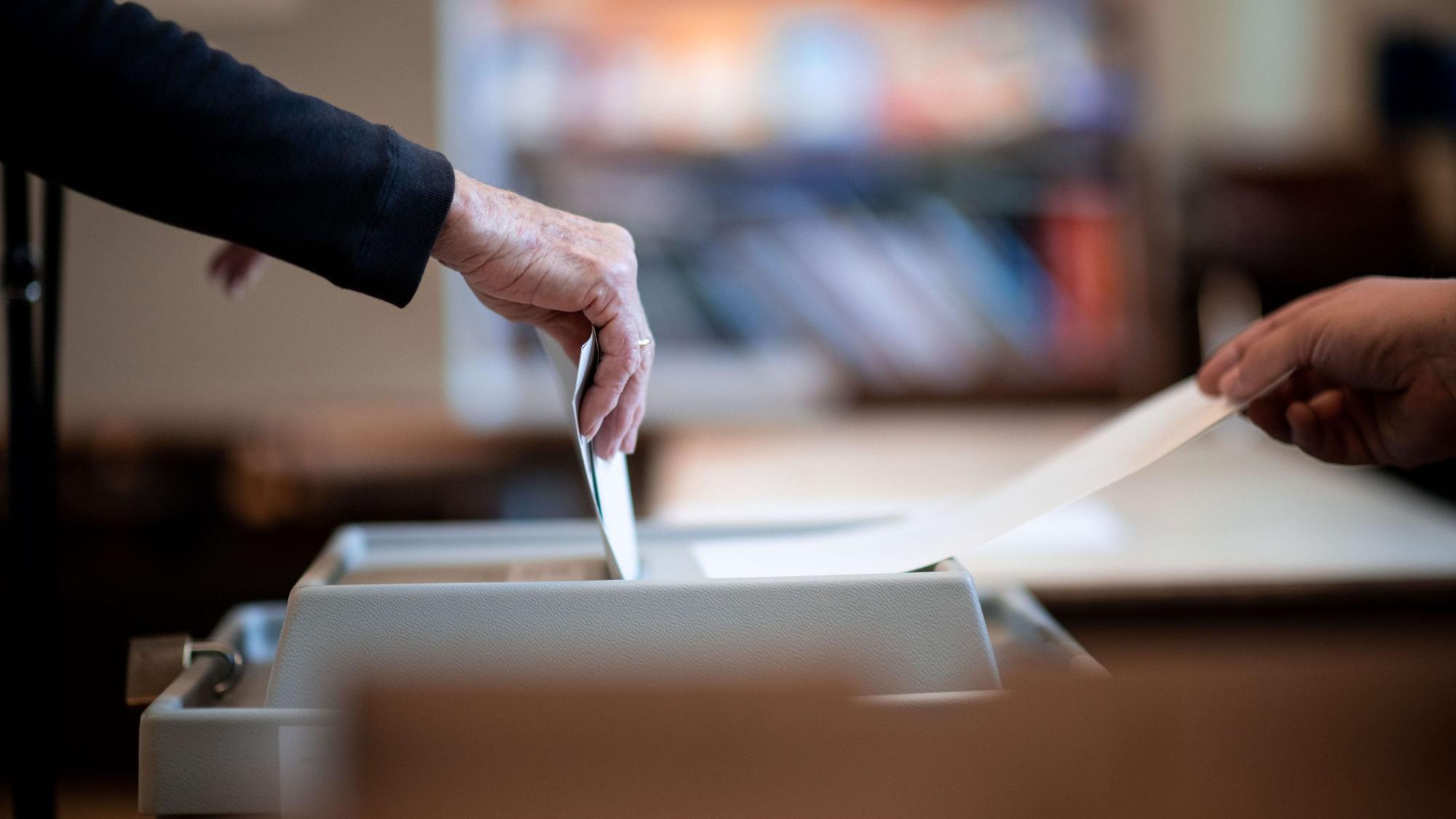 Eine Person wirft einen versiegelten Wahlzettel in eine Wahlurne.