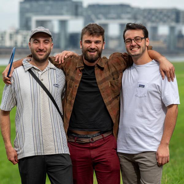 Andreas Stickelmann, Simon Heuser und Leonard Träger stehen auf den Poller Wiesen, im Hintergrund die Kranhäuser.