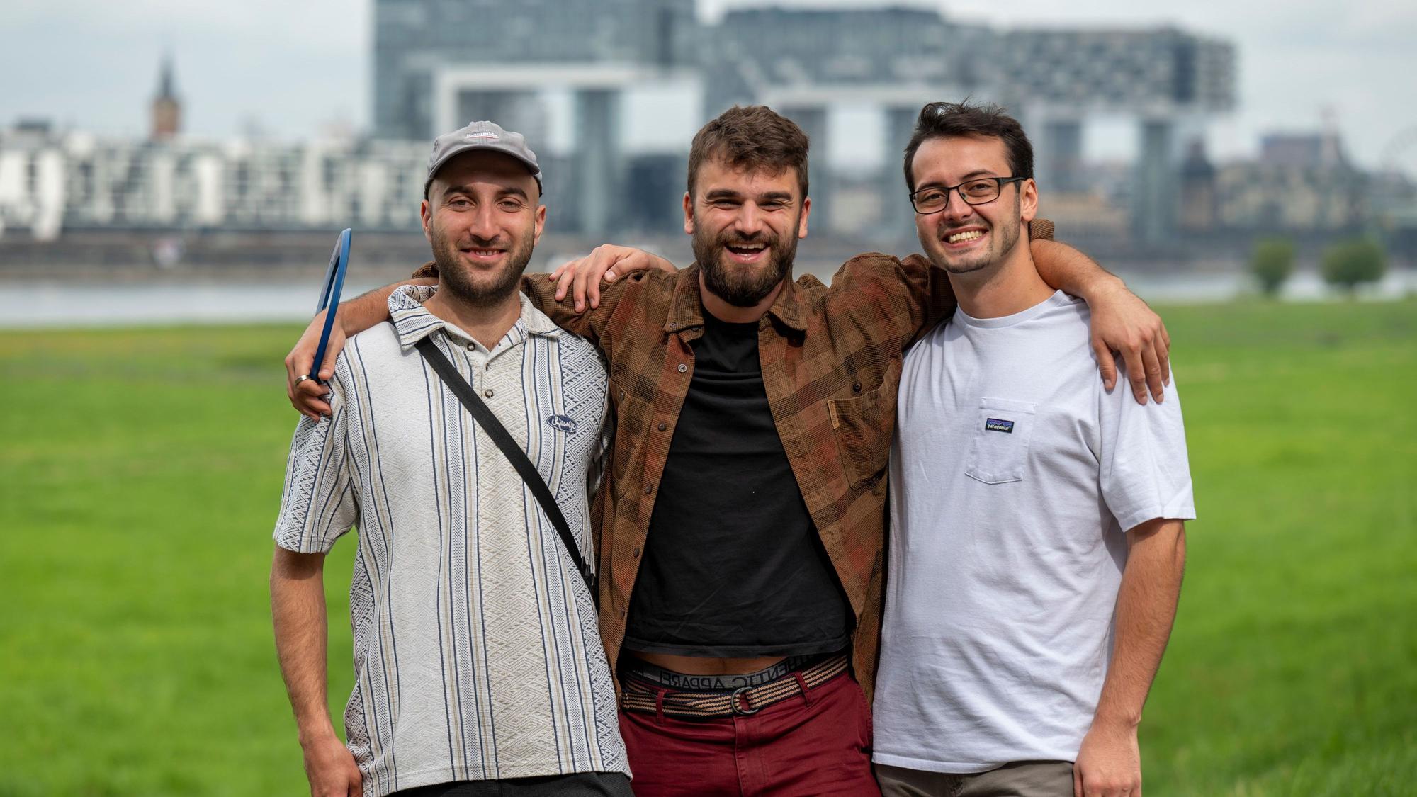 Andreas Stickelmann, Simon Heuser und Leonard Träger stehen auf den Poller Wiesen, im Hintergrund die Kranhäuser.