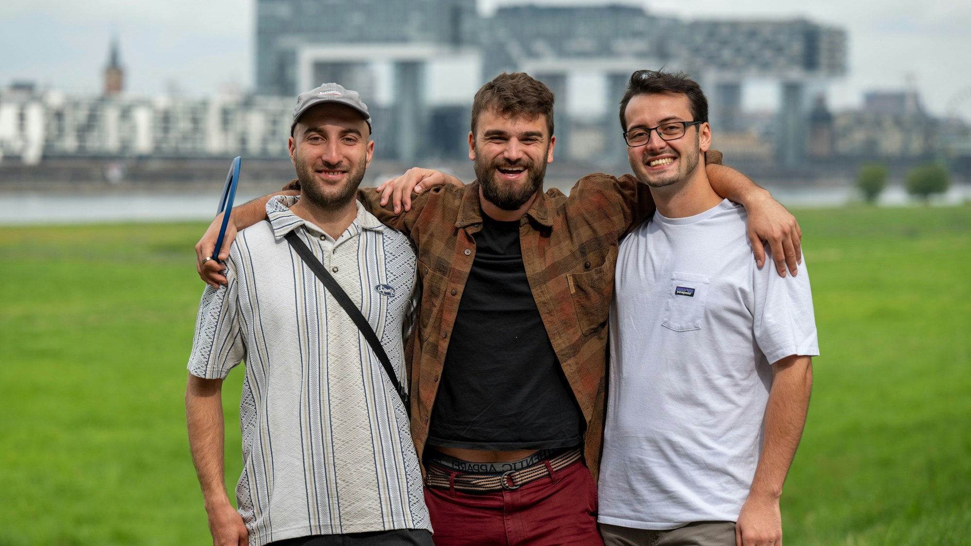Andreas Stickelmann, Simon Heuser und Leonard Träger stehen auf den Poller Wiesen, im Hintergrund die Kranhäuser.