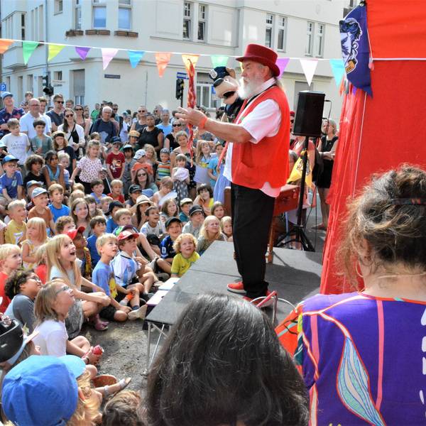 TEin Puppenspieler mit einer Handpuppe steht auf einer Bühne vor zahlreichen Kindern.