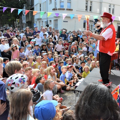 TEin Puppenspieler mit einer Handpuppe steht auf einer Bühne vor zahlreichen Kindern.