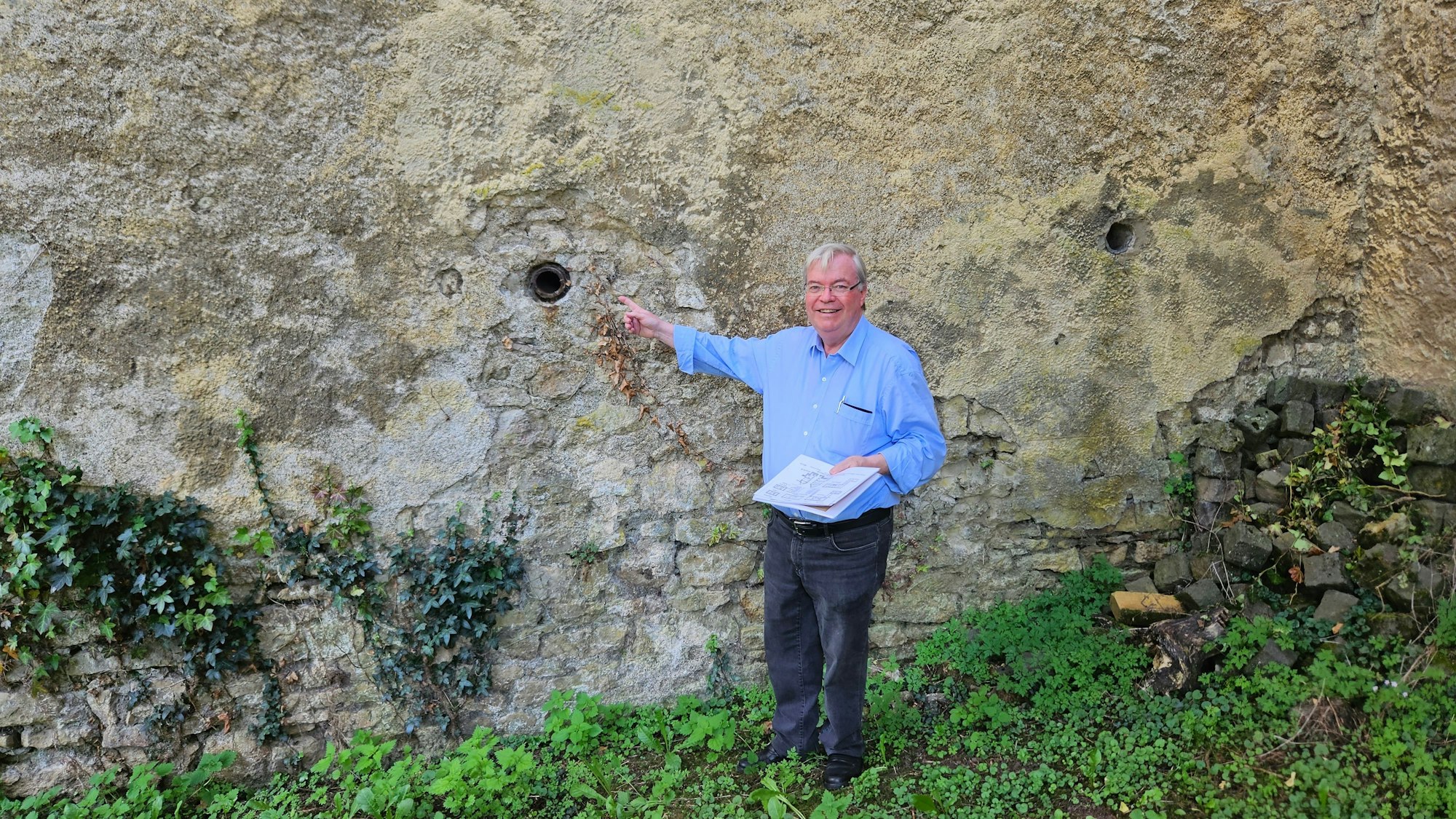 Der Historiker Helmut J. Kirfel zeigt auf eine Rohröffnung in einer Außenwand.