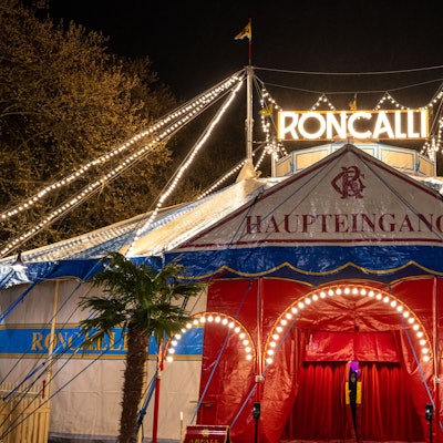 Das Roncalli-Zirkuszelt mit beleuchtetem Schriftzug am Abend ist zu sehen.