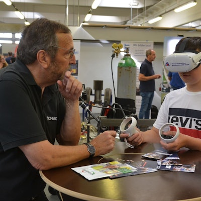 Der Neuntklässler Noah Gerhards trägt eine VR-Brille und hält in jeder Hand eine Bedienkonsole. Metallbaumeister Wilfried Schneider erklärt ihm, wie die Technik in die Ausbildung eingebunden werden kann.