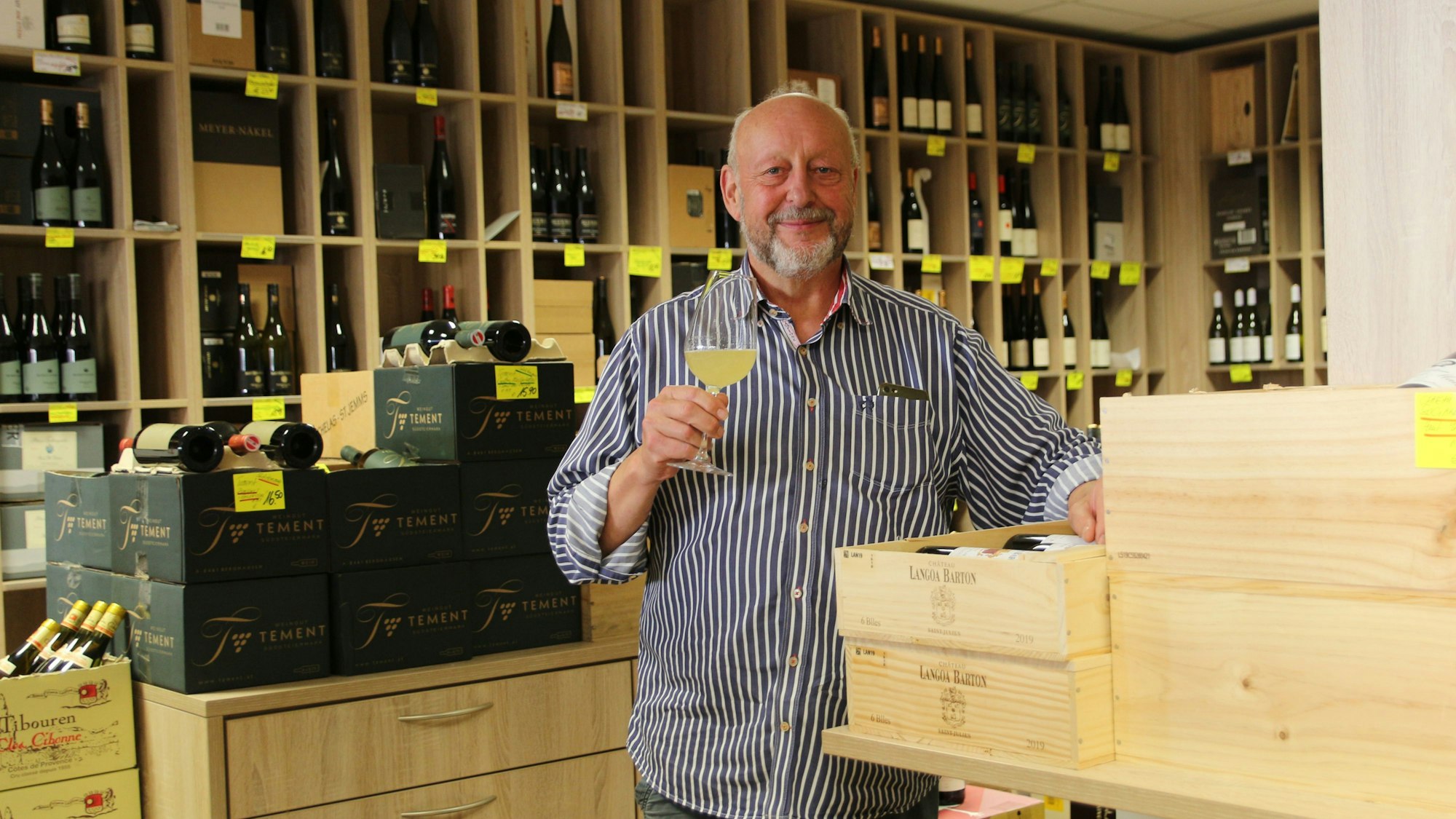 Ein Mann steht zwischen Weinkisten und hält ein Weinglas in der Hand.