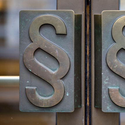 Außenansicht einer Gerichtstüre. Auf den Griffen sind Paragrafen zu sehen.