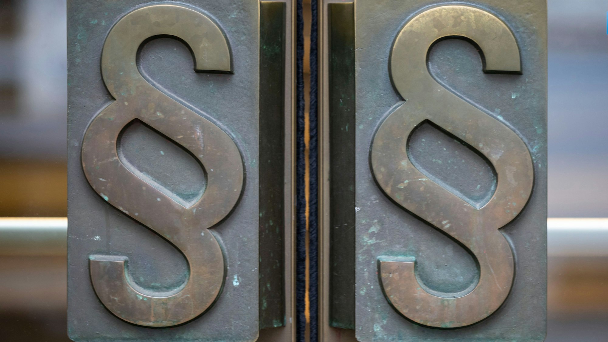 Außenansicht einer Gerichtstüre. Auf den Griffen sind Paragrafen zu sehen.