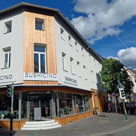 Ein weiß gestrichenes Gebäude an einer Straßenecke. Auf großen Schildern steht der Name des Lokals.