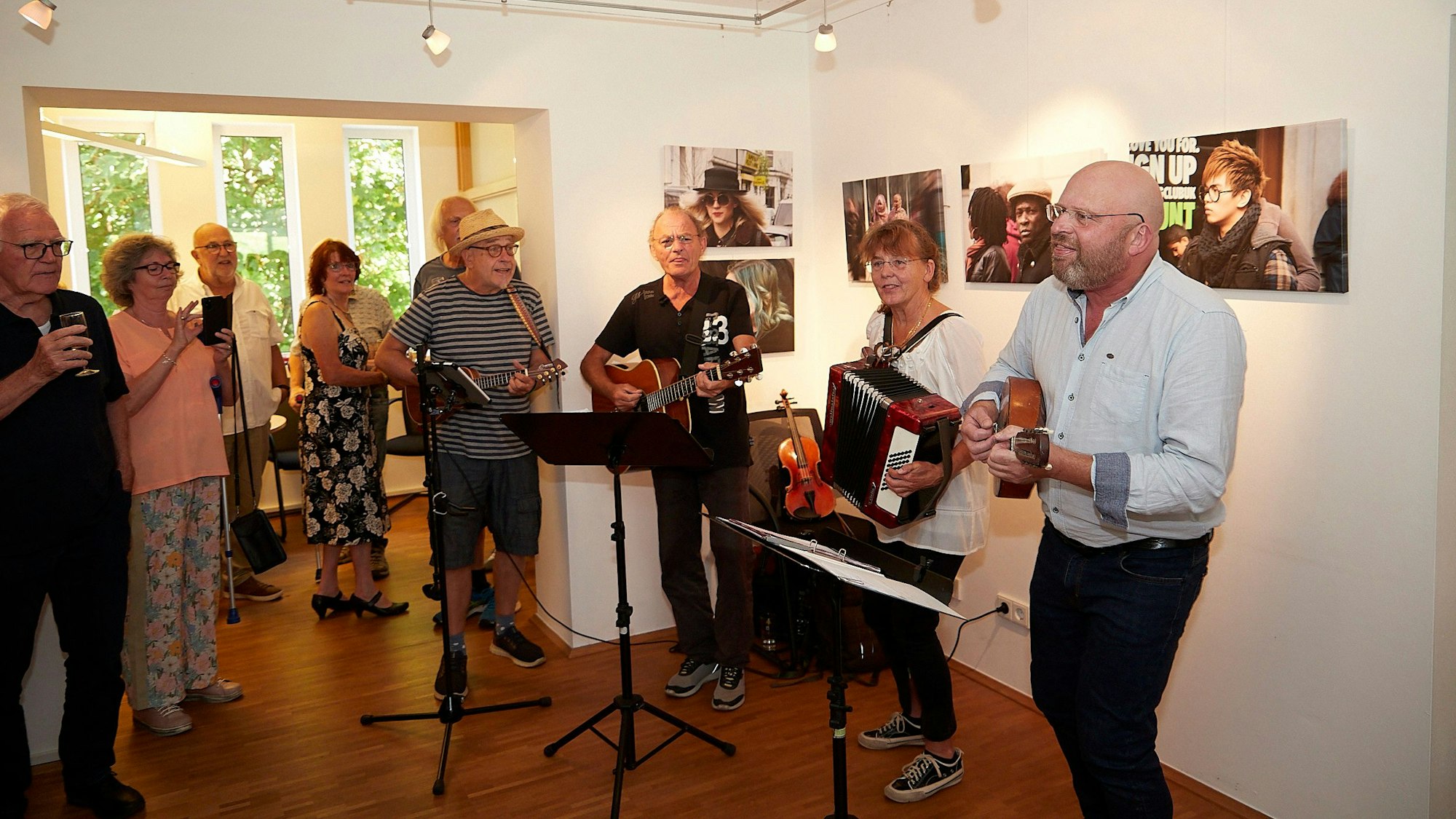 Die Band Cantalyra spielt, einige Leute stehen dabei und klatschen. Im Hintergrund sind einige Bilder einer Fotoausstellung zu sehen.