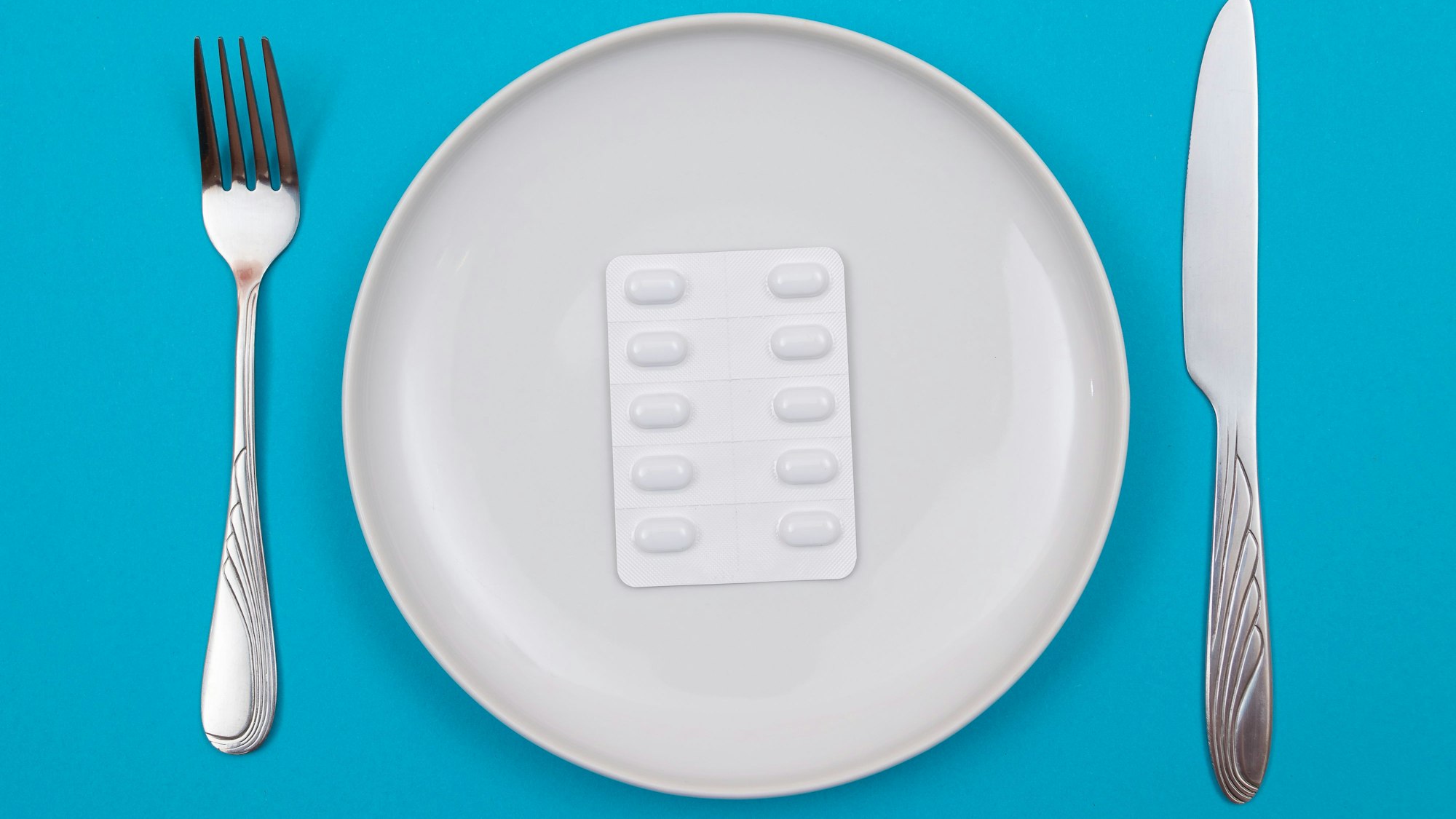 Tablettenpackung auf einem Teller mit Messer und Gabel daneben