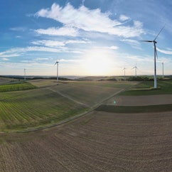 Windkraftanlagen stehen in einer Landschaft mit Feldern und Wäldern.