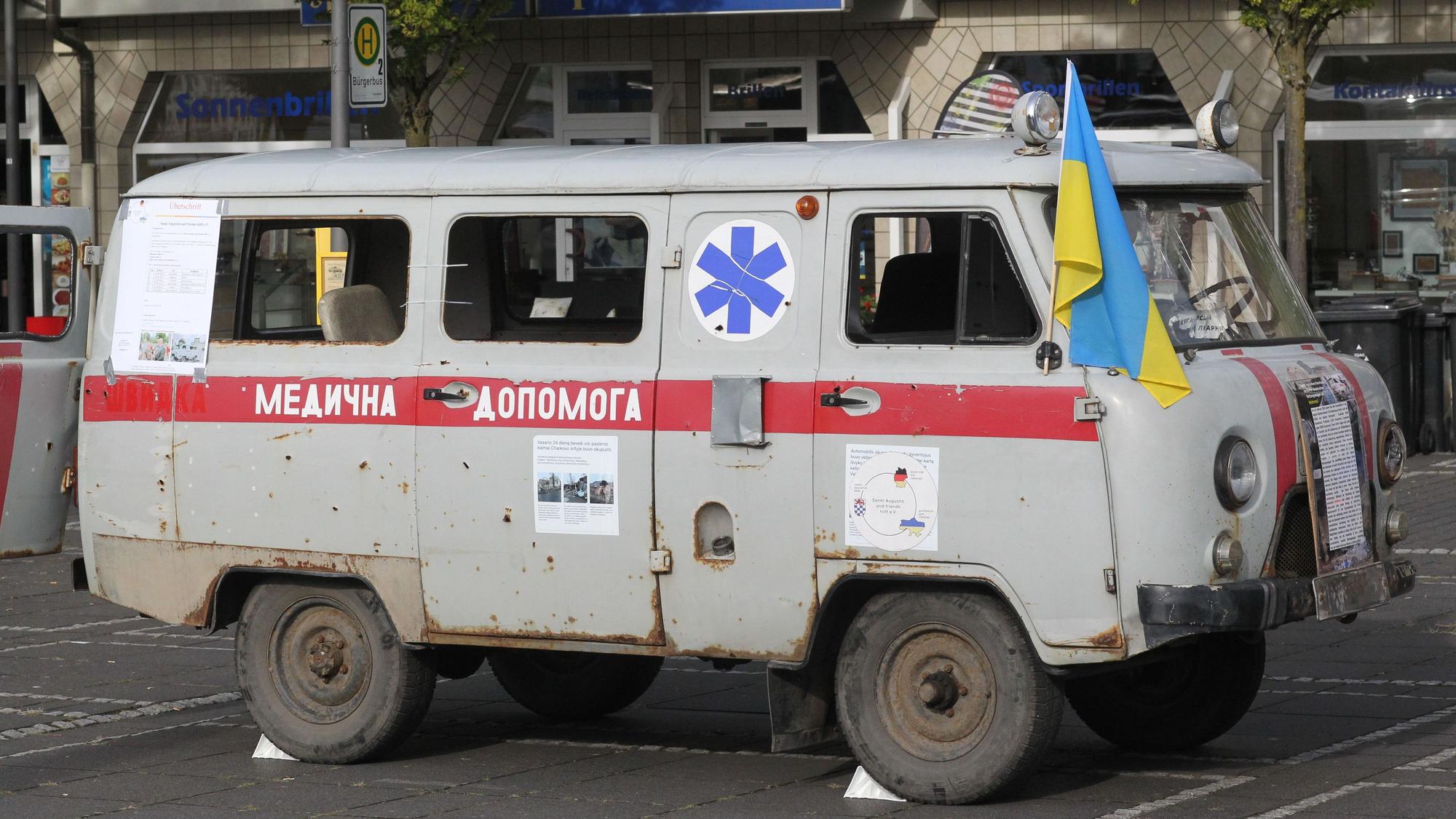 Ein beschossener ukrainischer RTW mit ukrainischer Flagge steht auf einem Platz im Rhein-Sieg-Kreis.