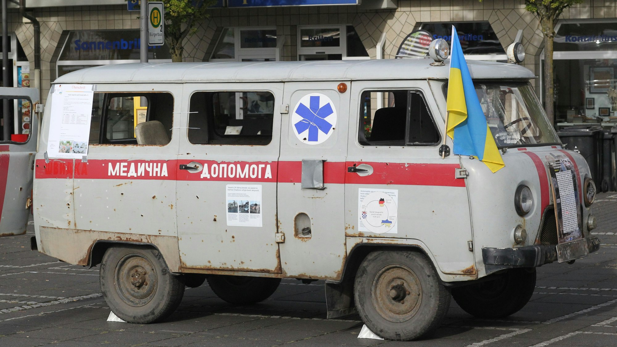Ein beschossener ukrainischer RTW mit ukrainischer Flagge steht auf einem Platz im Rhein-Sieg-Kreis.