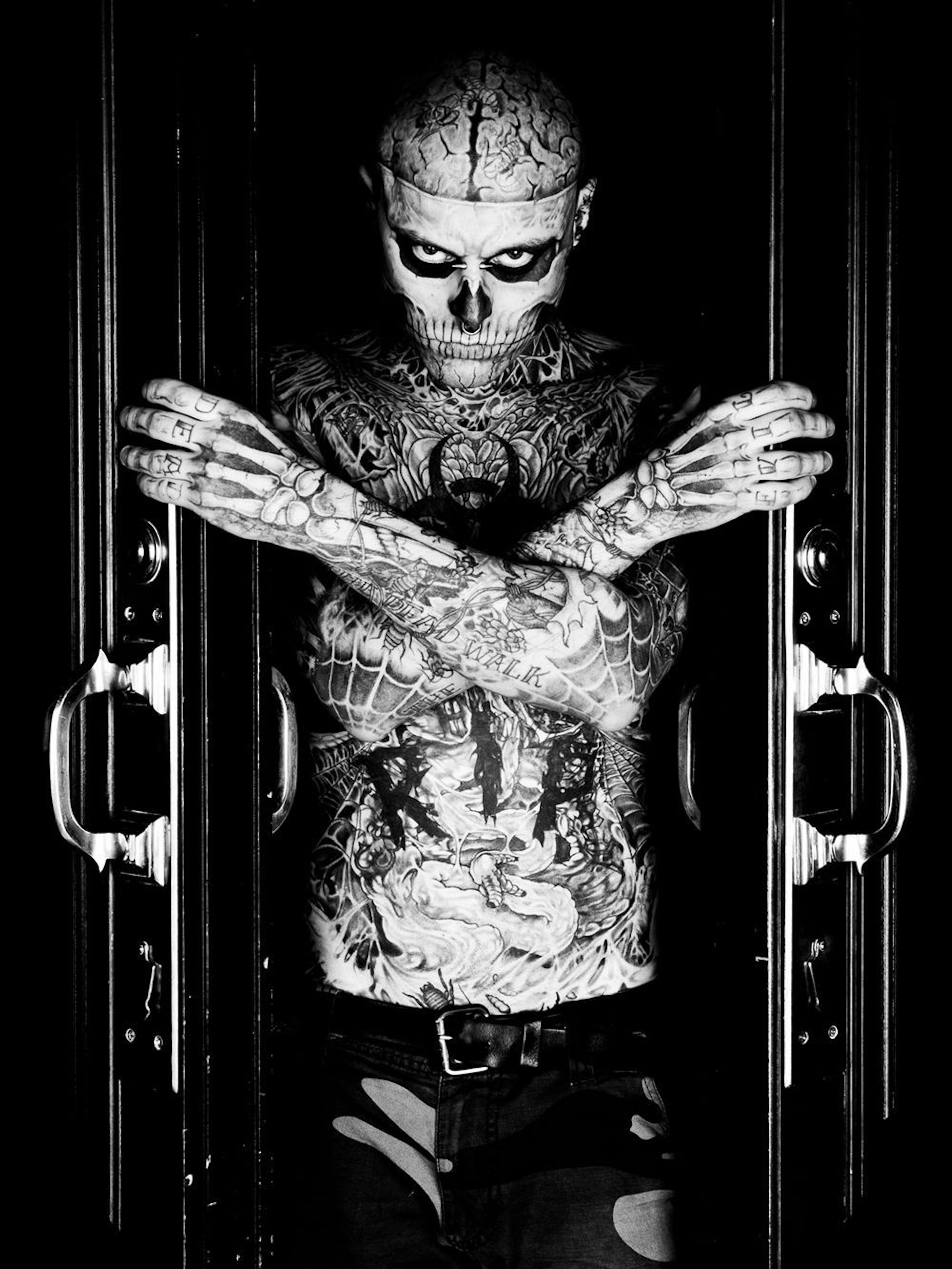 Ein junger Mann mit ins Gesicht tätowiertem Totenkopf schaut in die Kamera.