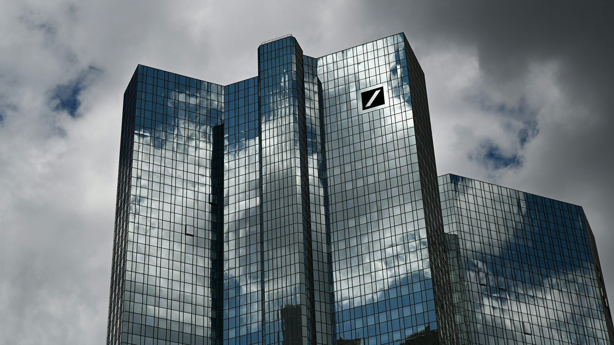 Hessen, Frankfurt/Main: Wolken ziehen über die Zentrale der Deutschen Bank, während sich der Wolkenhimmel in der Fassade spiegelt. (Symbolbild/Archivbild)