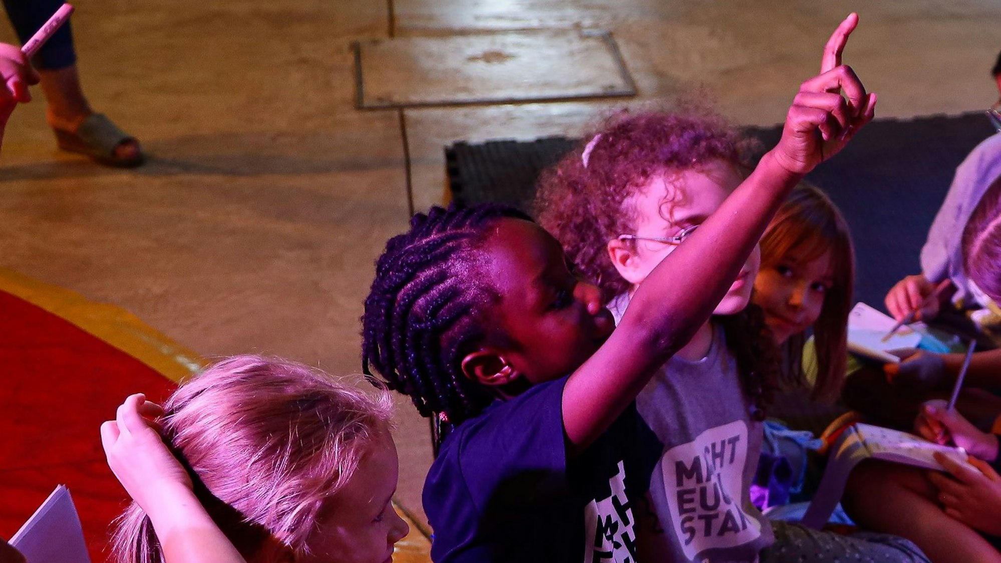 Ein Mädchen sind auf dem Boden einer Manege und hebt den Finger in die Luft, es ist ein Mitglied des Kinderrats des Kölner Linoclubs, bei dem Mitbestimmung und Teilhabe groß geschrieben werden.