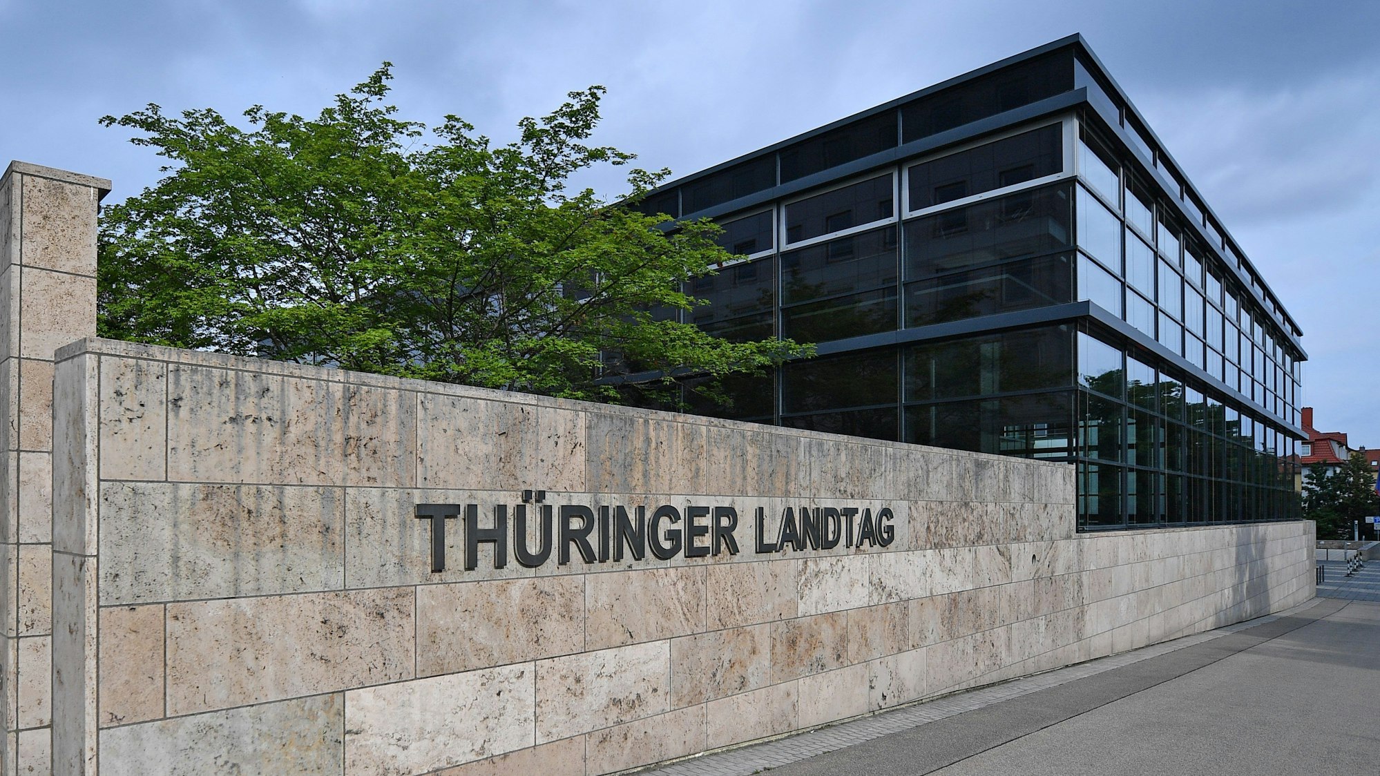 Das Foto zeigt ein modernes Gebäude des Thüringer Landtags, vor dem sich eine niedrige Sandsteinmauer mit der Aufschrift „Thüringer Landtag“ befindet.