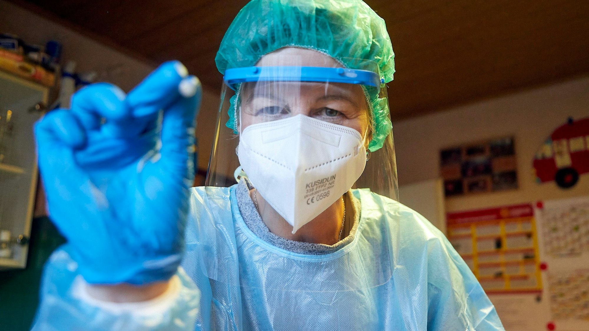 Das Archivbild zeigt eine Person in einem Schutzanzug, die ein Teststäbchen in die Höhe hält.