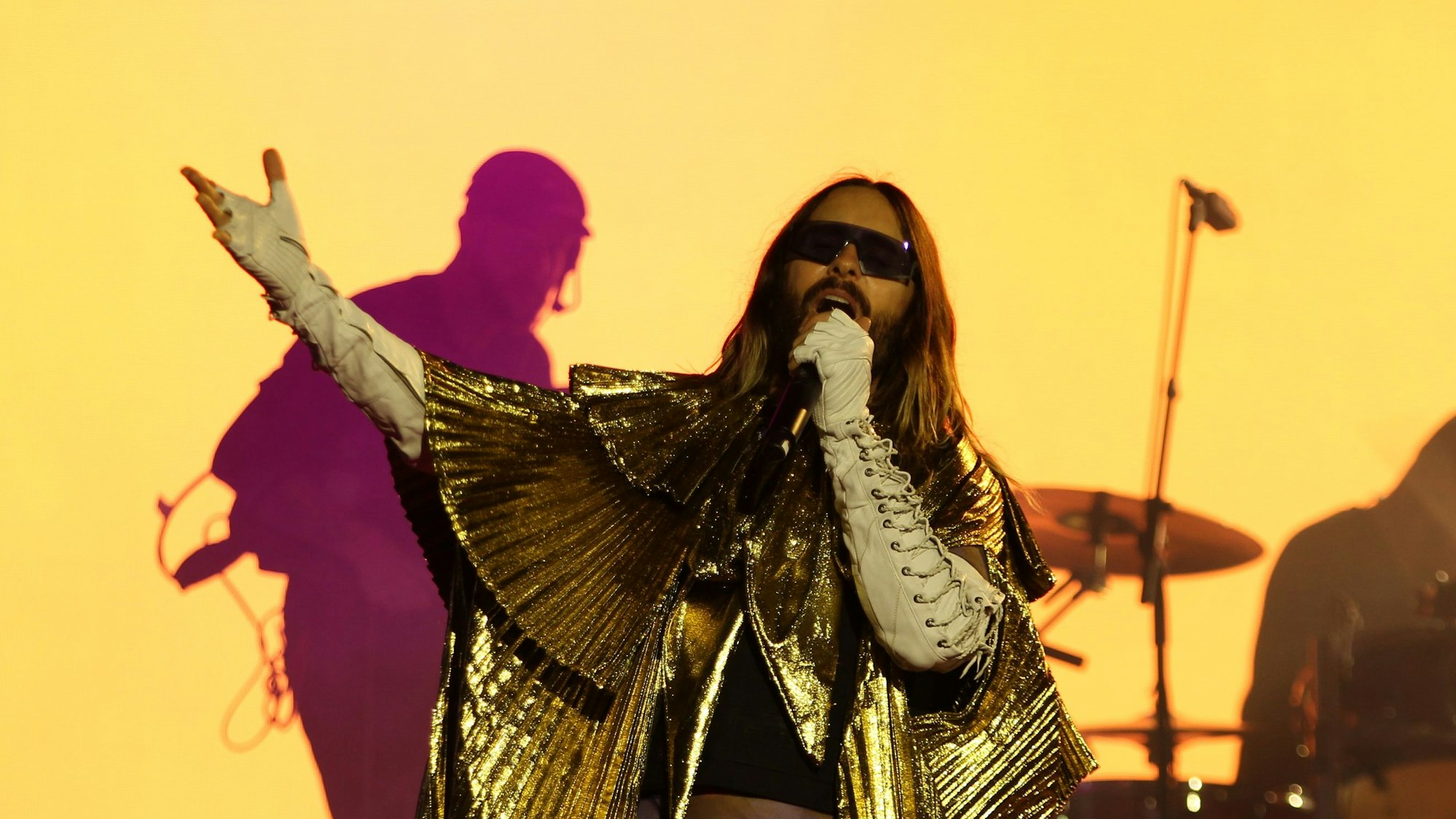 Sänger Jared Leto posiert im goldenen Umhang. Im Hintergrund sieht man die Silhouette seines Bruders Shannon am Schlagzeug.