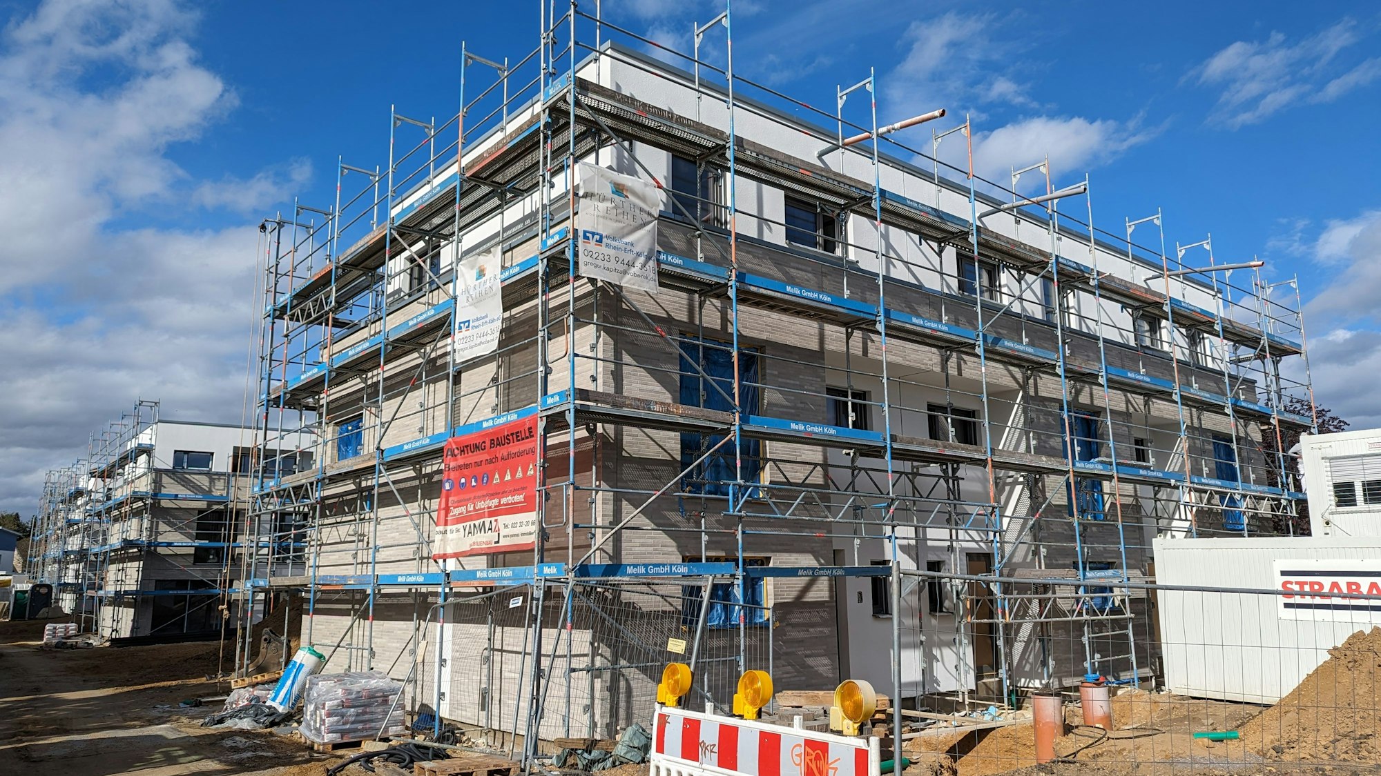 Ein Haus in der Bauphase. Rund um das Haus ist ein Gerüst aufgebaut. Im Hintergrund weitere Häuser mit Gerüsten.