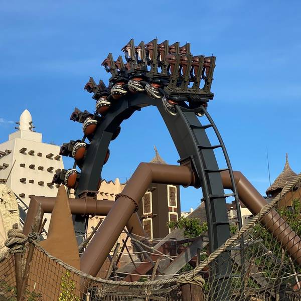 Die Achterbahn Black Mamba im Phantasialand fährt durch einen Looping. Im Hintergrund sieht man die Themenwelt „Deep in Africa“.