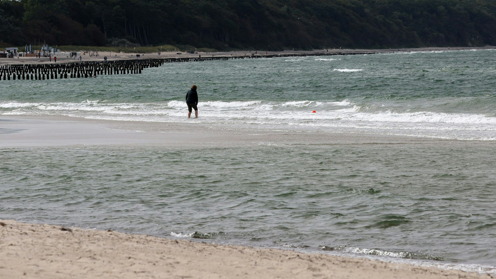 Ein Spaziergänger geht am Strand in Warnemünde bei Rostock ins Wasser. Im Hintergrund sind kleinere Wellen in der Ostsee zu sehen. (Symbolbild)