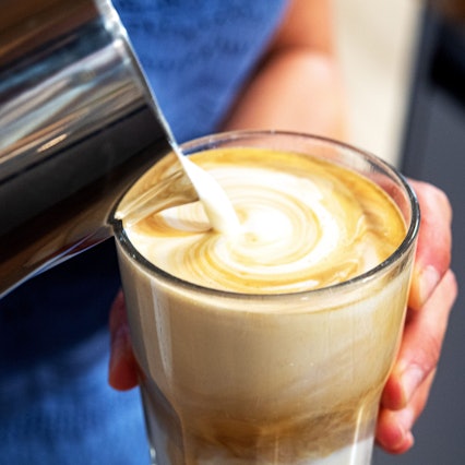 Cremige Milch wird in ein Glas mit Kaffee geschüttet.