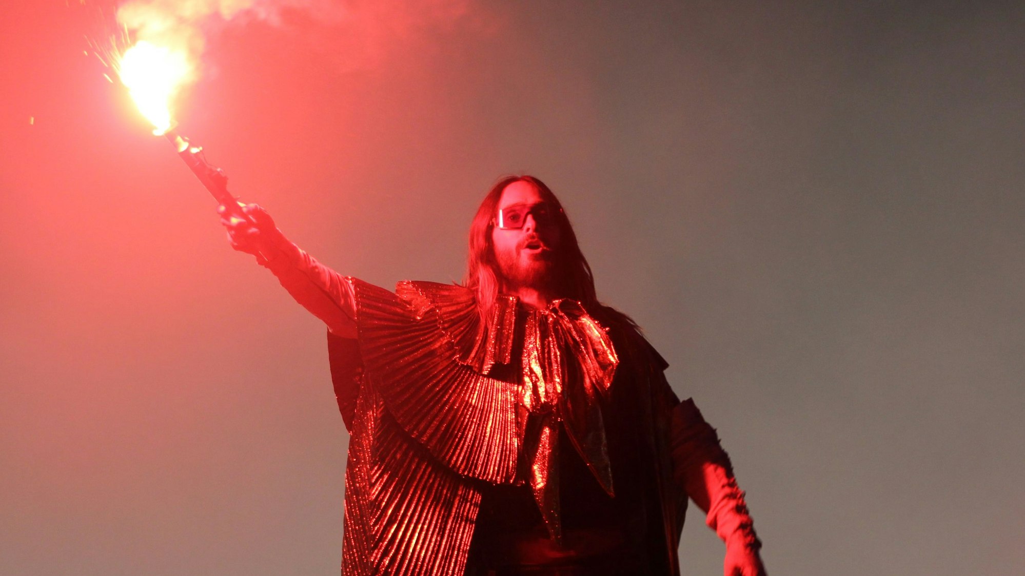 Sänger Jared Leto stet mit einer brennenden bengalischen Fackel in der Hand in Rauchschwaden.