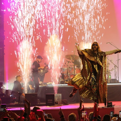 Sänger Jared Leto tanzt am Bühnenrand, während im Hintergrund ein Funkenstrahl aus dem Boden schießt.