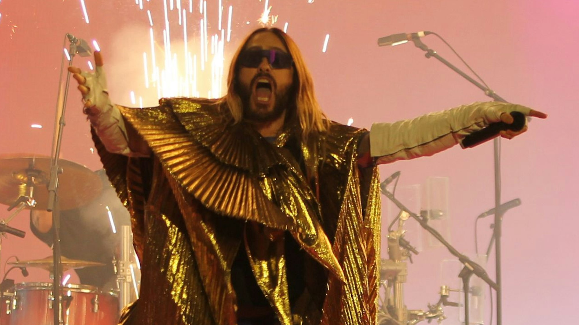 Sänger Jared Leto tanzt am Bühnenrand, während im Hintergrund ein Funkenstrahl aus dem Boden schießt.