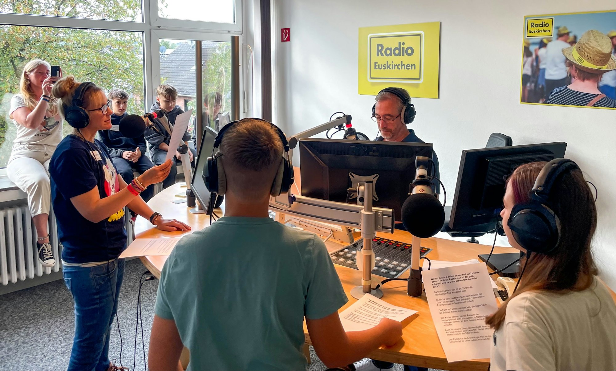 Norbert Jeub, Chefredakteur von Radio Euskirchen, am Mikrofon. Er wird umringt von den jungen Besuchern und weiteren Redakteuren.