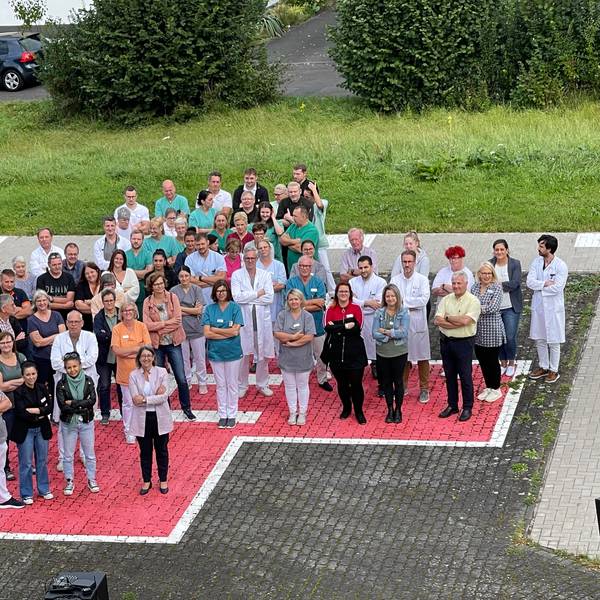 Menschen stehen mit verschränkten Armen auf einem auf das Pflaster aufgemalten roten Kreuz.