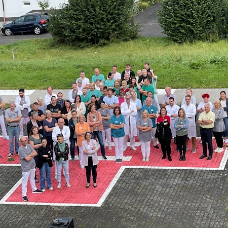 Menschen stehen mit verschränkten Armen auf einem auf das Pflaster aufgemalten roten Kreuz.