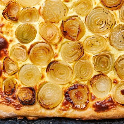 Zwiebelkuchen liegt auf einem Backblech.