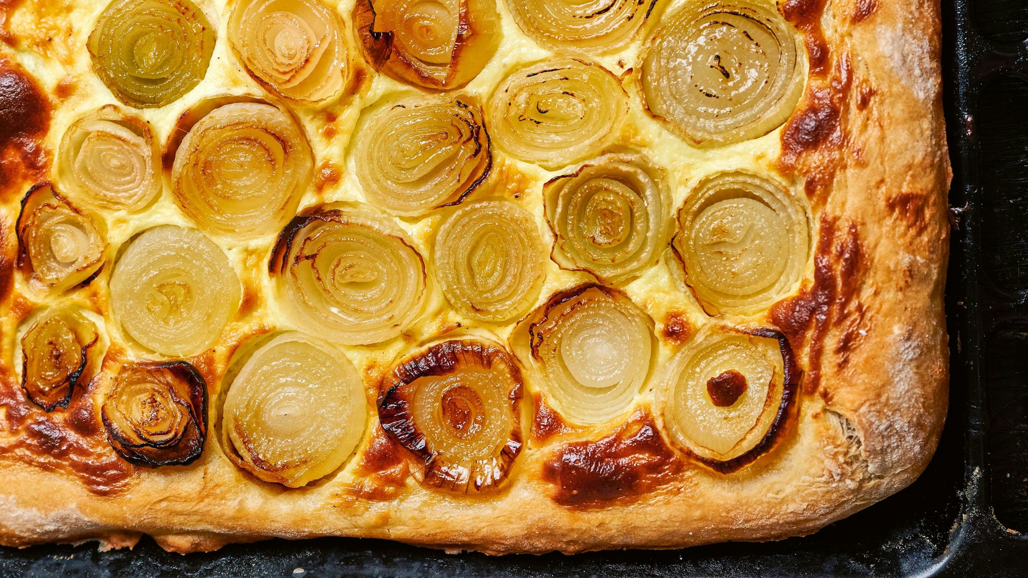 Zwiebelkuchen liegt auf einem Backblech.