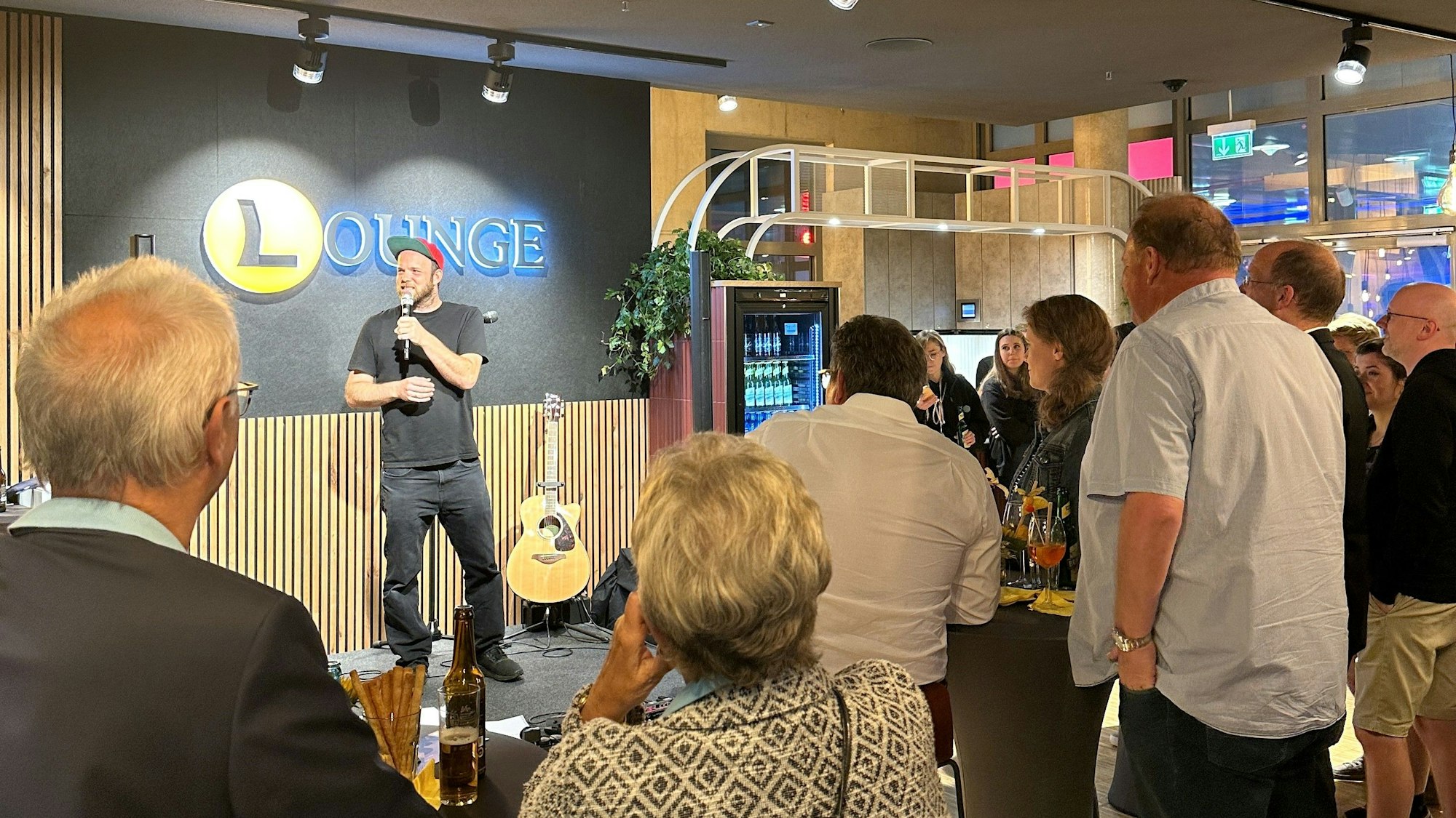 Ein Mann steht auf der Bühne, mehrere Leute schauen ihm zu.