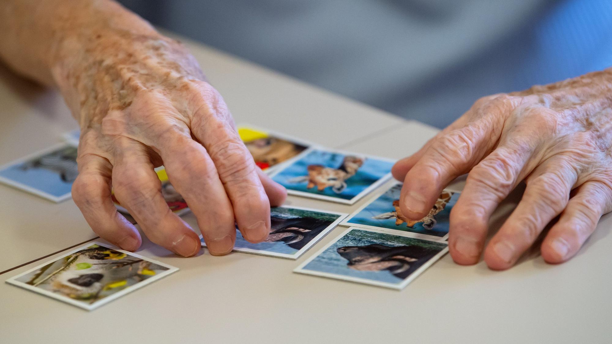 Eine Bewohnerin eines Altenheims spielt auf einer Pflegestation Memory und legt Kartenpaare zusammen.