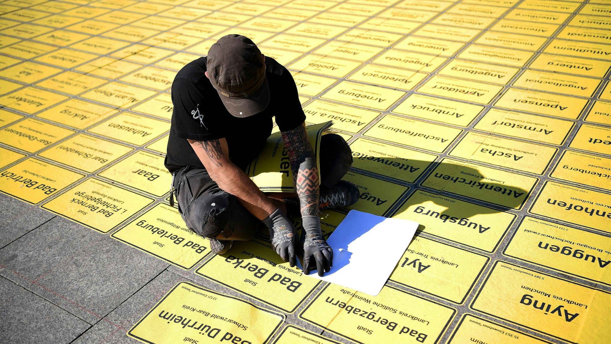 Ein Mann klebt Ortseingangsschilder auf den Gehweg (Archivfoto).