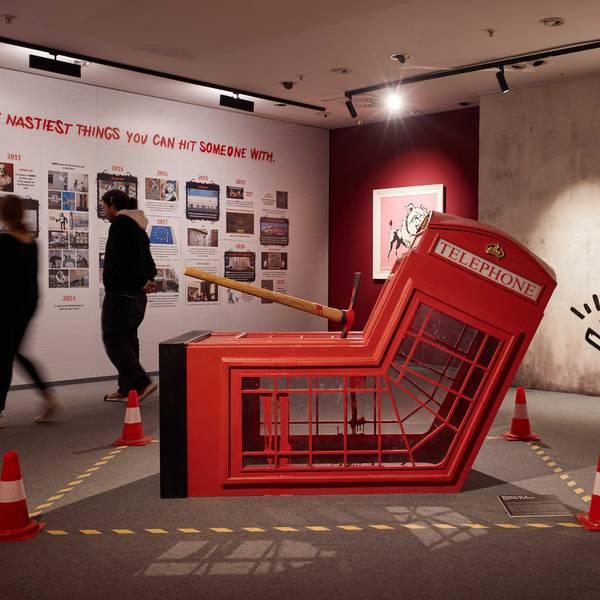 Mitarbeiter gehen in der Ausstellung "The Mystery of Banksy - A Genius Mind". Im Vordergrund ist die Installation "Death Of Telephone Booth" zu sehen.