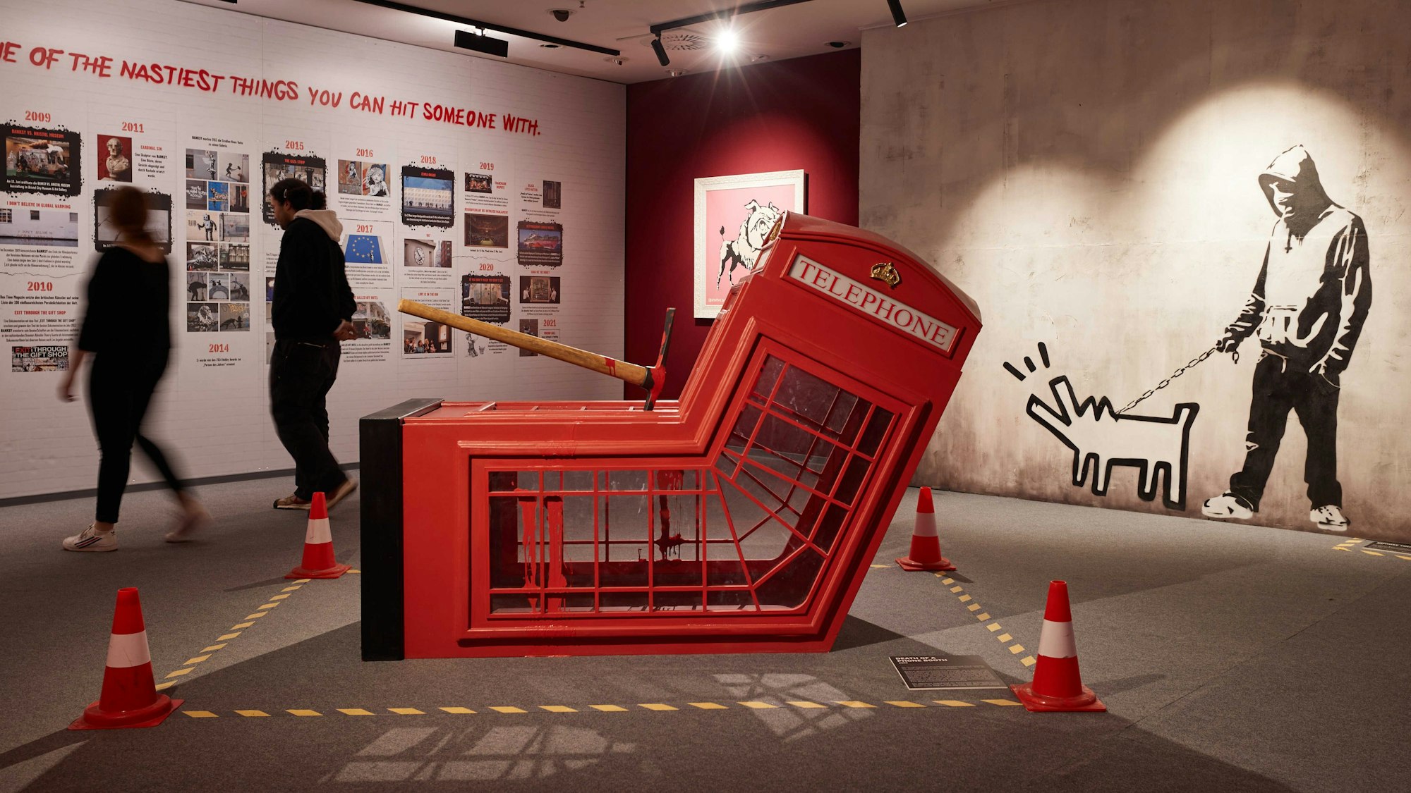 Mitarbeiter gehen in der Ausstellung "The Mystery of Banksy - A Genius Mind". Im Vordergrund ist die Installation "Death Of Telephone Booth" zu sehen.