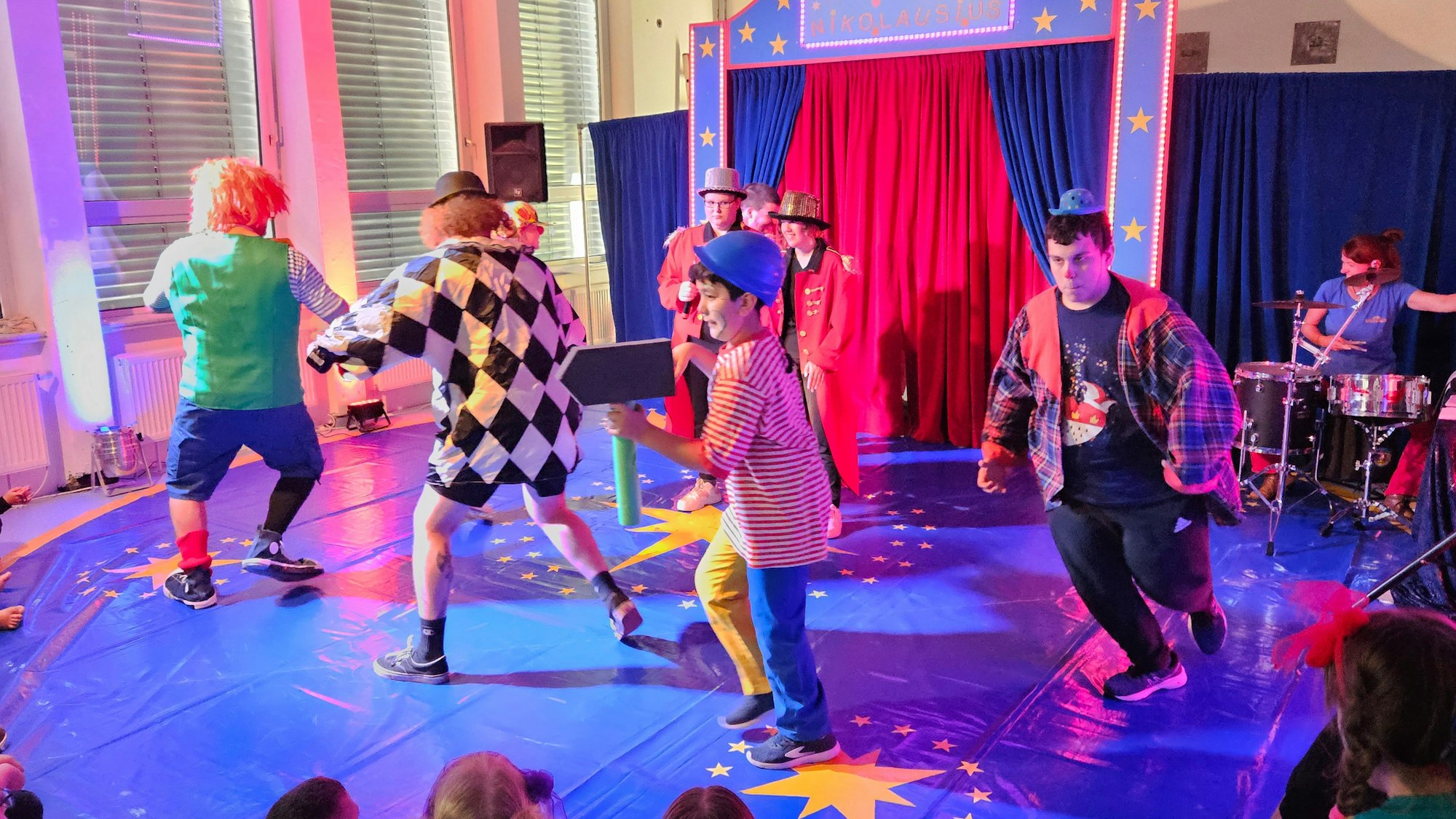 Bunt kostümierte Erwachsene und Jugendliche laufen in einer kleinen Zirkusmanege im Kreis.