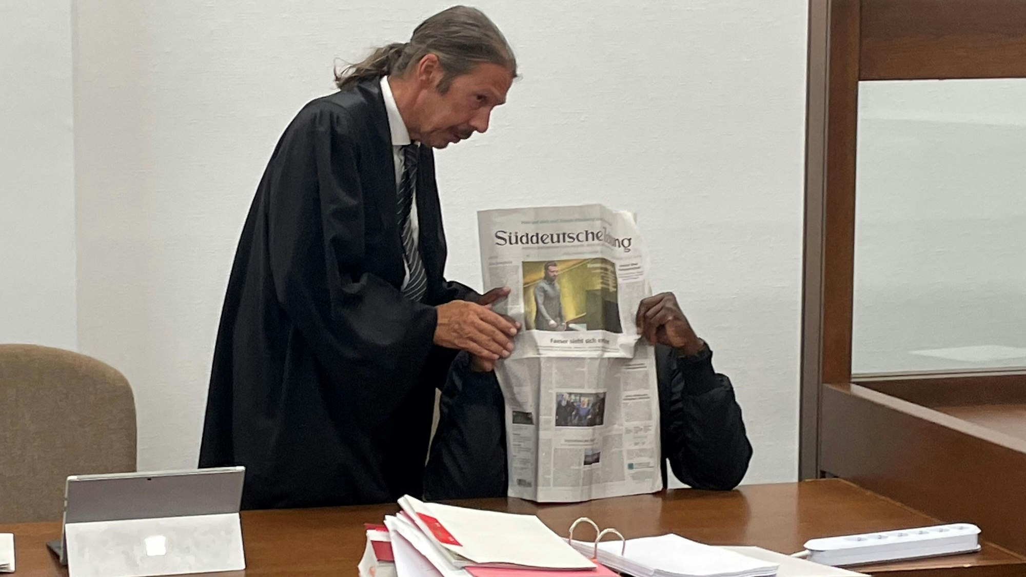 Der Angeklagte versteckt sich hinter der Zeitung seines Verteidigers Ingo Lindemann.