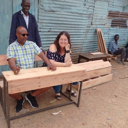 Das Bild zeigt einen Mann und eine Frau, die an einer Schulbank sitzen